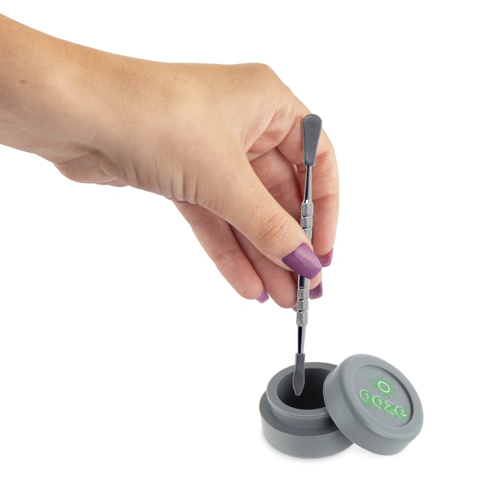 A hand holds the Ooze Fusion Atomizer Vape Battery, revealing its compact size and metallic finish next to a dark cap.