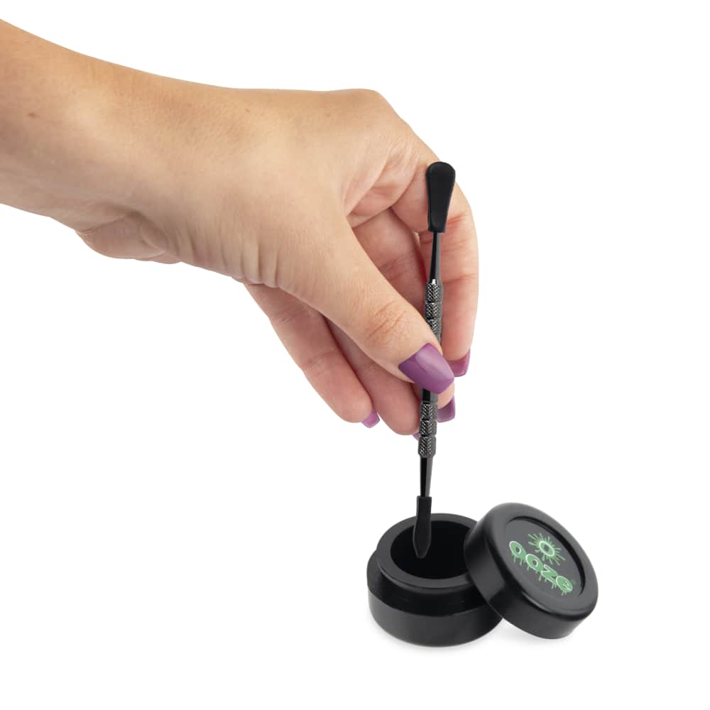 A hand holds the Ooze Fusion Atomizer Vape Battery next to its charging base, seen from a slightly elevated angle.
