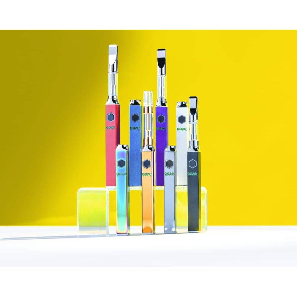 A studio shot displays several square Ooze Quad 510 Thread 500 mAh Vape Pen Batteries in various colors, lined up against a plain white background.