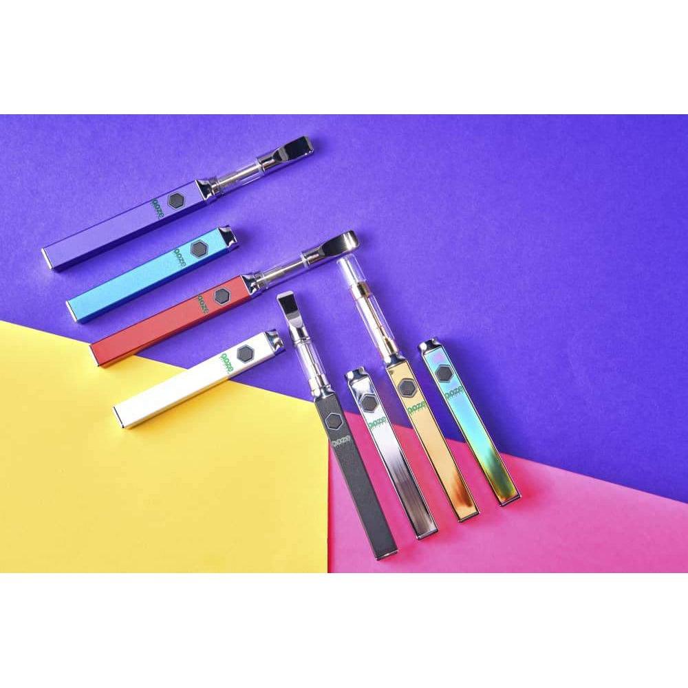 A flat lay showcases several colorful Ooze Quad 510 Thread 500 mAh Square Vape Pen Batteries arranged diagonally on a dark surface.