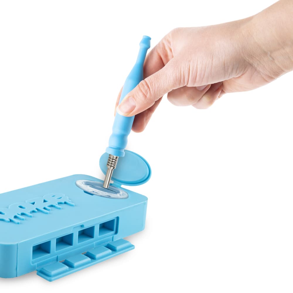 A hand holds a cleaning pick over the open, blue Ooze Slugger Silicone Dugout, revealing its segmented interior.