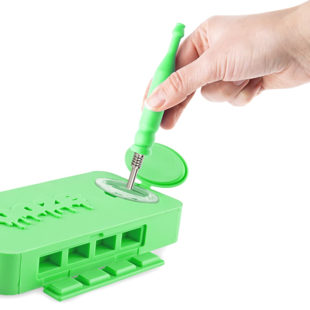 A hand holds a tool over the open, green silicone dugout of the Ooze Slugger, revealing its internal compartments.