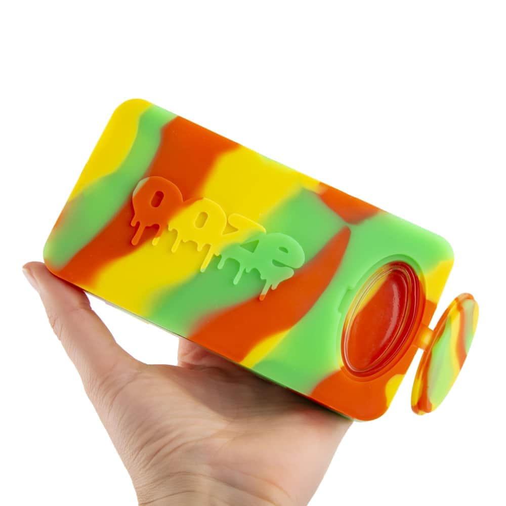 A hand holds the Ooze Slugger Silicone Dugout, showcasing its colorful, compact design in a bright, angled view.