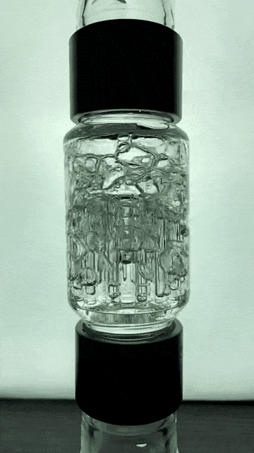 Vertical close-up of the Prism Water Pipes Rasta Beaker Triple Stack showing its clear stacked chambers and internal percolator details against a softly lit background