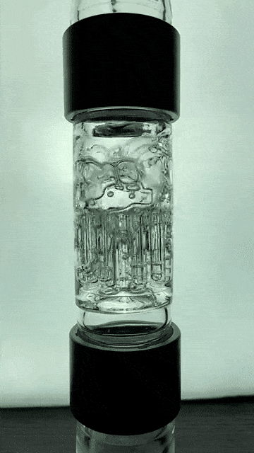 Vertical close-up of the glass section of the Prism Water Pipes Rasta Beaker Triple Stack showing stacked percolators and textured chambers between black silicone bands.