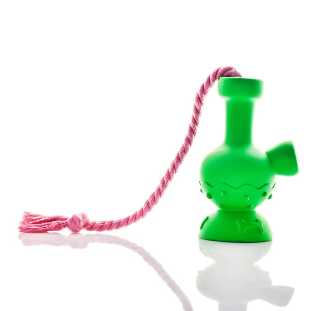 Right-side view of a bright green Tug & Toke toy with a curved neck and short spout, sitting on a reflective white surface with a twisted pink rope draped over its top.