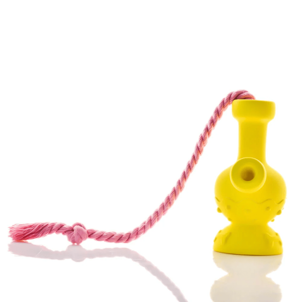 Bright studio side view of the yellow Tug & Toke with a twisted pink rope looped through its top, reflected on the white surface.