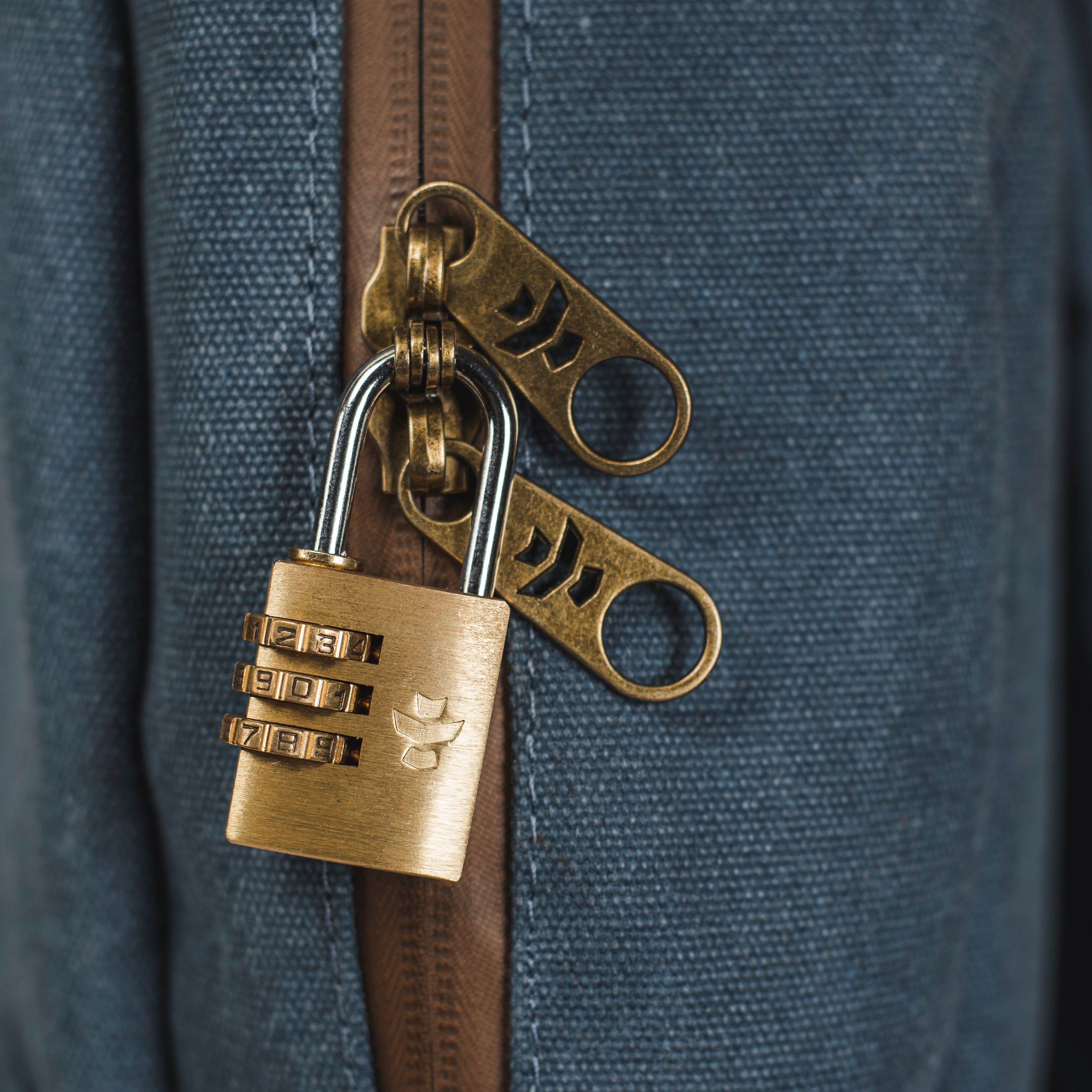 Close-up view of The Explorer - Smell Proof Backpack’s zipper pull, featuring a bronze-colored, numbered lock attached to it.