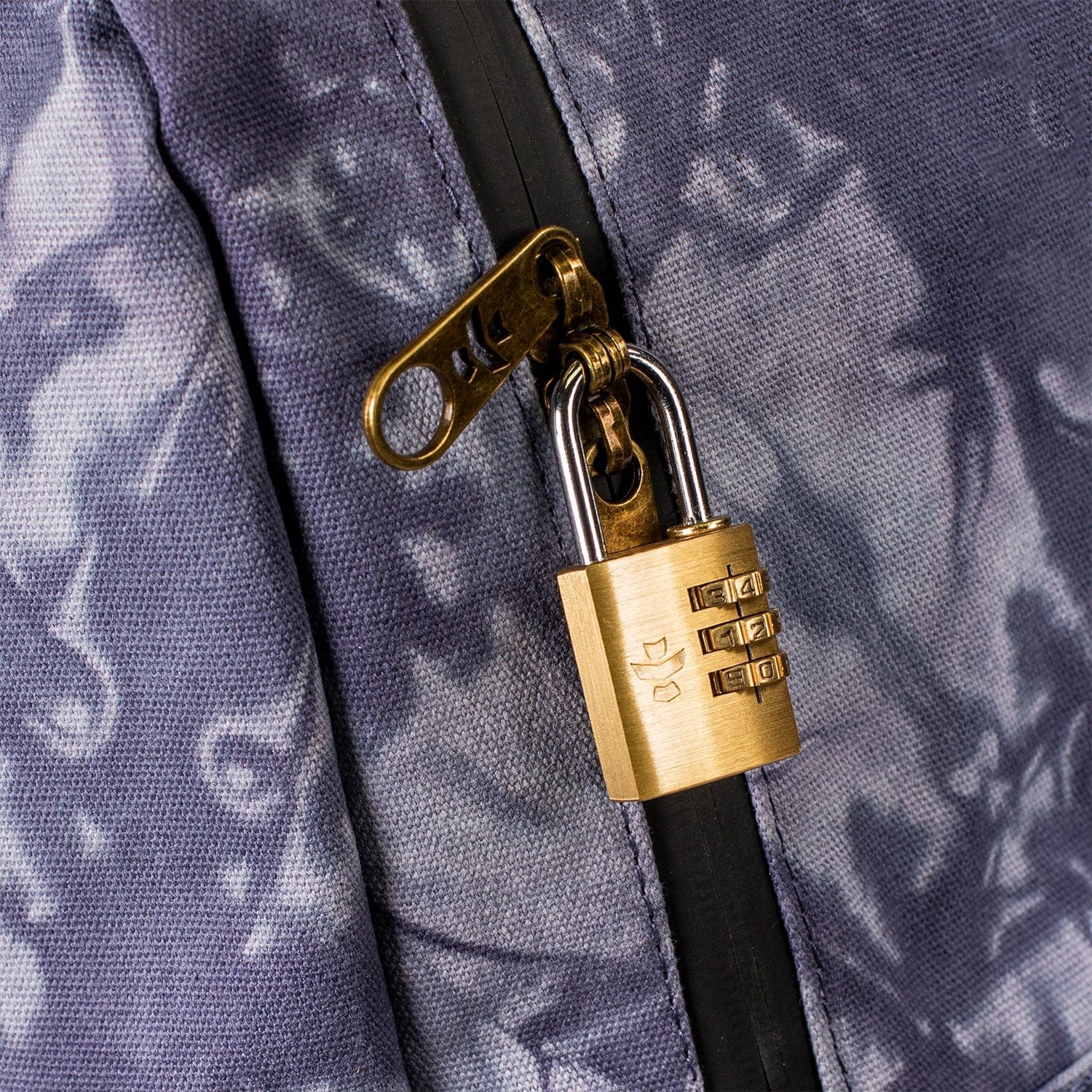 Close-up of The Explorer - Smell Proof Backpack’s zipper pull, revealing a silver and gold lock mechanism against a textured backdrop.