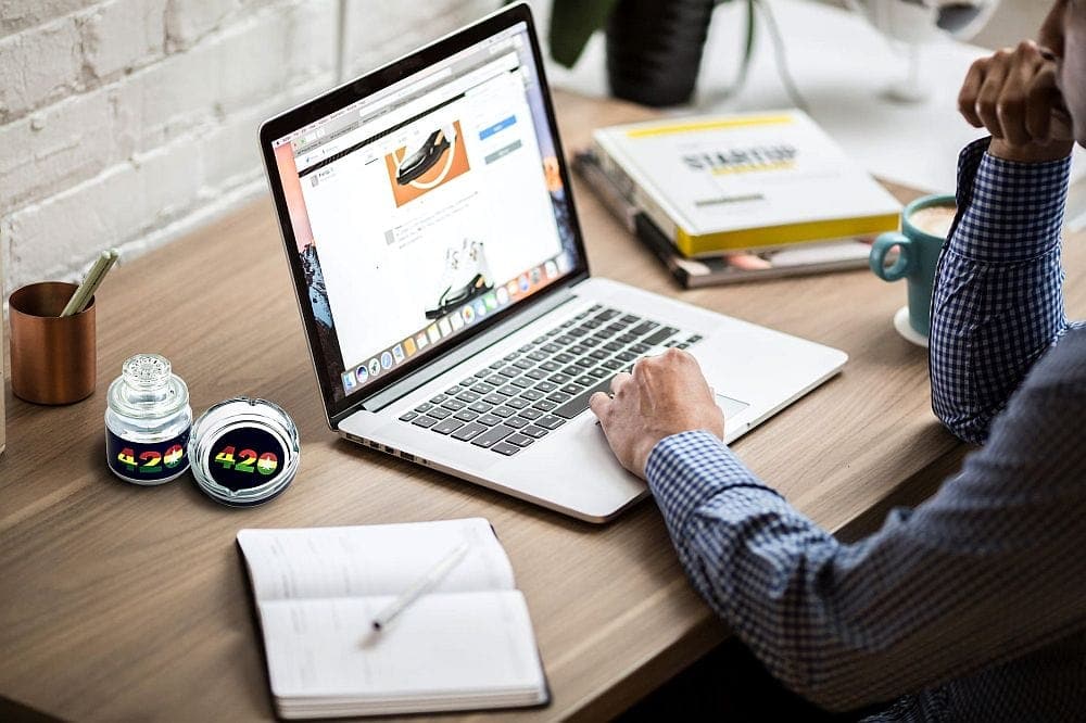 Overhead view of a laptop next to the **Ashtray set with Stash jar - 420 DESIGN**, alongside a notebook and coffee cup on a wooden table.