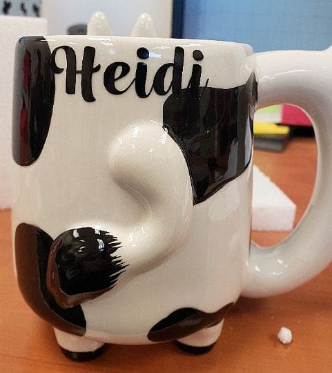 Close-up, front view of the Cow Pipe Mug, a white ceramic mug with a whimsical cow design.