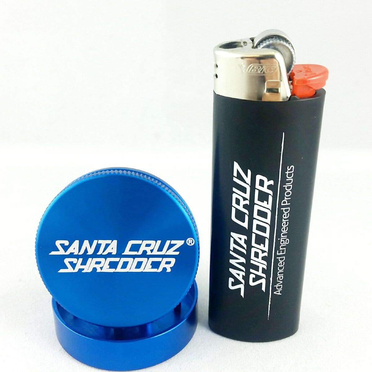 A close-up shows the two-piece Santa Cruz Shredder Mini Grinder in a metallic blue finish, angled slightly against a dark background.