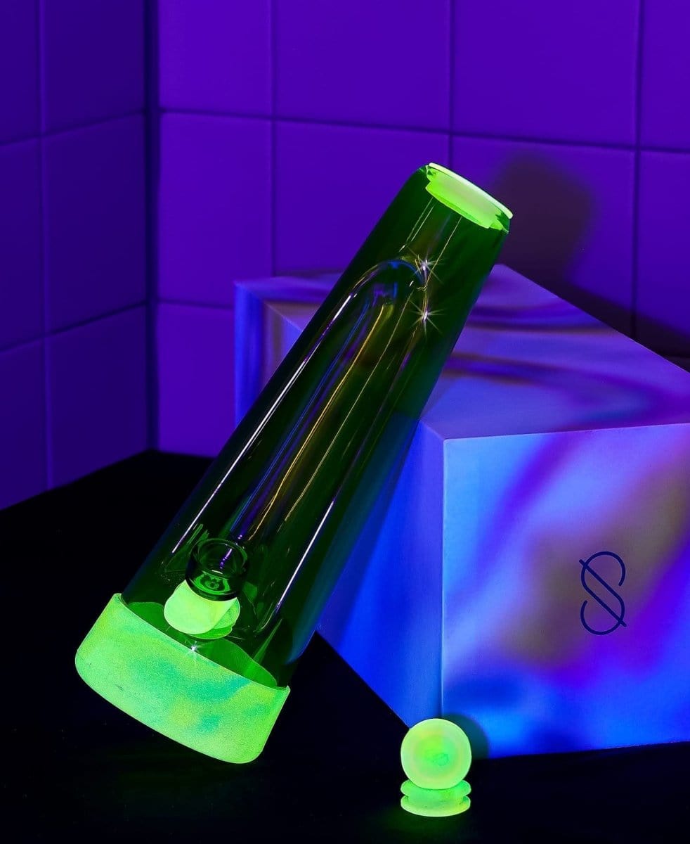 A brightly lit, front view of the Designer Bong GLOW on a blue reflective surface.