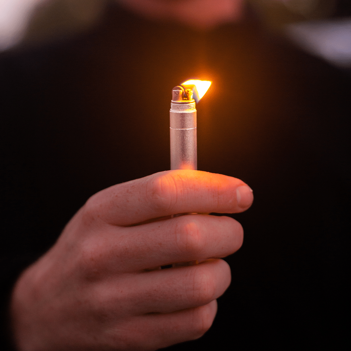 A close-up, angled view shows the lit StashLight - Doob Tube & Refillable Lighter held in a hand, emitting a bright flame.