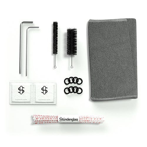 Top-down view of the Stündenglass Gravity Infuser accessory kit laid out on white, showing allen keys, two bottle brushes, a gray microfiber cloth, O-rings, cleaning wipes, and a branded pipe cleaner.